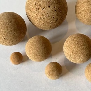 May include: A set of eight cork balls of varying sizes, ranging from small to large. The balls are all natural cork color and have a rough, textured surface.