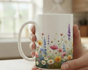 May include: White ceramic mug with a floral design featuring colorful wildflowers. The mug is filled with a hot beverage, with steam rising from the top. The mug is held by two hands.