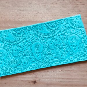May include: A turquoise blue silicone baking mat with a paisley pattern. The mat is designed for use with fondant, gum paste, and other edible decorations.
