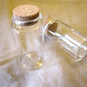 May include: Two clear glass bottles with cork stoppers. The bottles are empty and have a round shape.