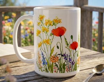 May include: A white ceramic mug featuring a colourful watercolour illustration of various wildflowers, including bright red poppies, yellow clusters, and small blue and orange blossoms, with a curved handle and a smooth, cylindrical body.