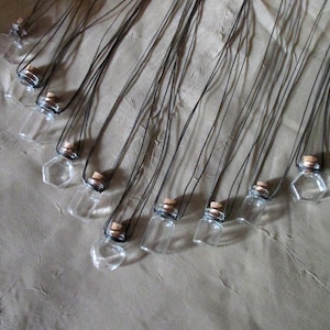 May include: A collection of small glass bottles with cork stoppers, each attached to a black cord. The bottles are arranged in a fan shape on a brown surface.