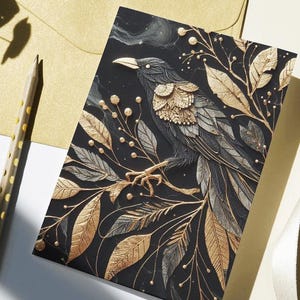 May include: A greeting card featuring a detailed illustration of a raven perched on a branch with gold and silver leaves. The raven has gold accents on its feathers, set against a dark background. A gold envelope and pencil are also visible.