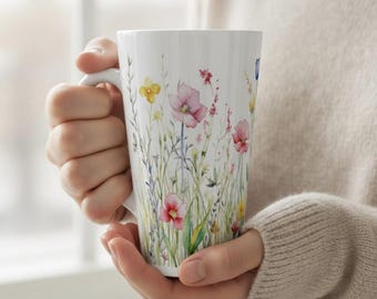 May include: A white ceramic mug with a black handle and the text "But First, Coffee" in a bold, black font. The mug is sitting on a wooden surface. The mug is approximately 4 inches tall.