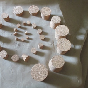 May include: A collection of cork stoppers of various sizes and shapes arranged in a spiral pattern on a light brown surface.