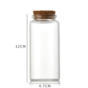 Może przedstawiać: Przezroczysta szklana butelka z korkowym korkiem. Butelka ma 12 cm wysokości i 4,7 cm szerokości.