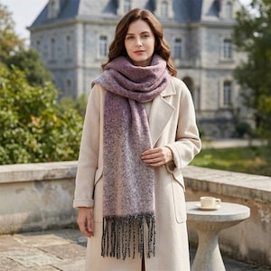 May include: A long, thick, textured scarf featuring a gradient color pattern that transitions from a deep purple at the top to a lighter, muted mauve and grey at the bottom, finished with long, dark grey fringe tassels at both ends.