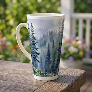 May include: A tall white ceramic latte mug featuring a wrap-around watercolor illustration of a dense pine forest. The design depicts layers of evergreen trees in shades of deep blue and green, fading into a soft, misty, and foggy atmosphere.