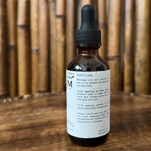 May include: A brown glass bottle with a black dropper top. The bottle has a white label with black text, including "HOW TO USE" and product information. The bottle is filled with a dark liquid.