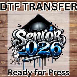 May include: DTF TRANSFER design featuring "Senior 2026" in a stylized font with blue accents, a graduation cap, and a pen. The design includes the text "Ready for Press" and a small robot graphic. The background is a wood grain pattern.