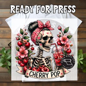 May include: A white t-shirt featuring a graphic of a skeleton wearing a red cherry-patterned headscarf, holding a red cherry drink. The design includes pink cherry blossoms, red cherries, and a banner with the text CHERRY POP.