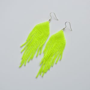 May include: A pair of neon yellow beaded fringe earrings featuring a triangular top section composed of small, uniform beads and long, dangling strands of matching neon yellow beads attached to silver-toned metal fishhook ear wires.