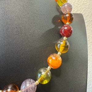 May include: A colorful beaded necklace featuring large, round beads in shades of orange, yellow, red, and purple. The beads are strung together with gold-colored connectors, creating a vibrant and eye-catching accessory.