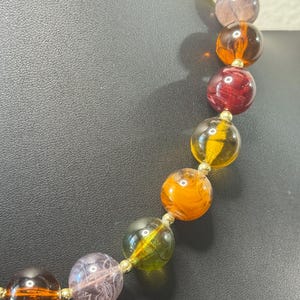May include: A colorful beaded necklace featuring large, round beads in shades of orange, yellow, green, purple, and red. The beads are strung together with gold-colored connectors, creating a vibrant and eye-catching accessory.
