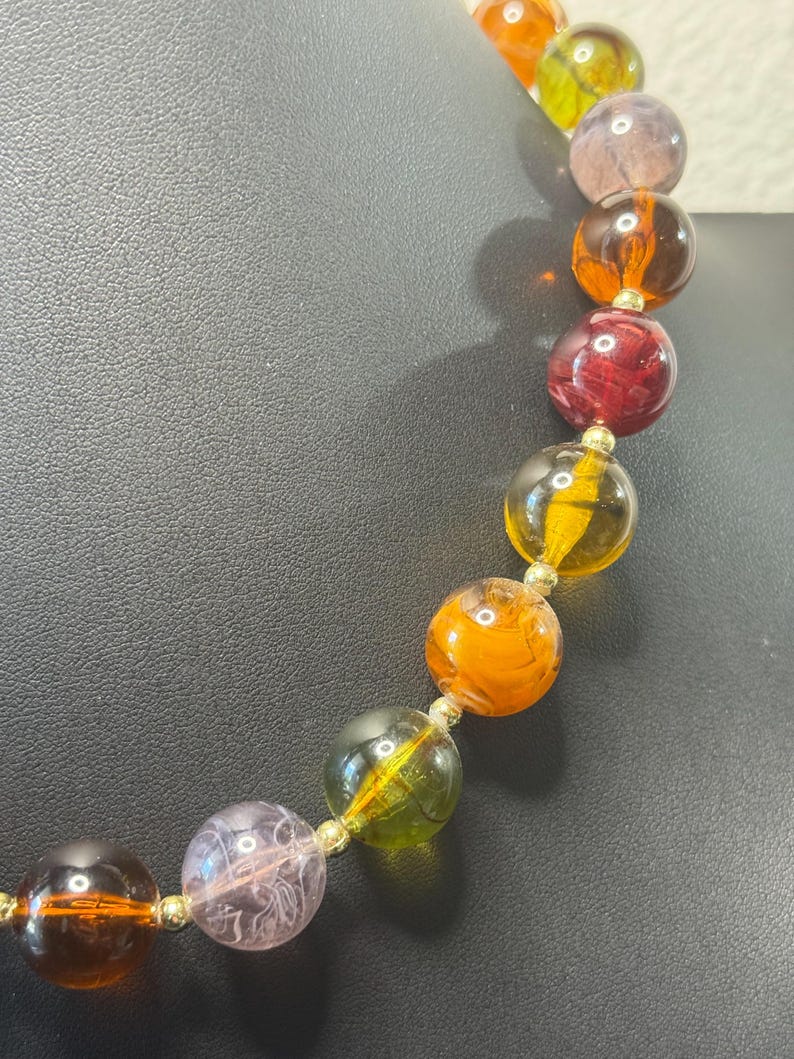 May include: A colorful beaded necklace featuring large, round beads in shades of orange, yellow, green, purple, and red. The beads are strung together with gold-colored connectors, creating a vibrant and eye-catching accessory.