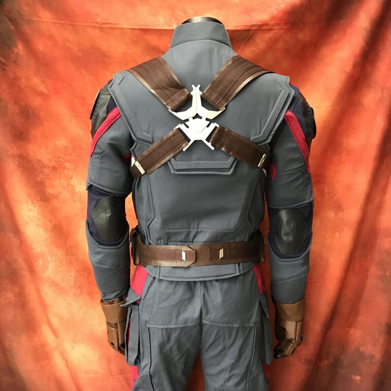 May include: A blue tactical costume jacket with dark red accents on the shoulders and sides. It features brown straps crossing the back, secured by a silver-colored metal emblem, and a brown utility belt around the waist with black elbow pads.