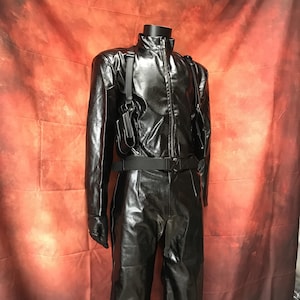Peut inclure: Un ensemble noir en similicuir sur un mannequin. L'ensemble comprend une veste zippée, un pantalon et une ceinture. Un étui est attaché à la veste. L'ensemble est présenté sur un fond rouge.