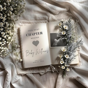 May include: An open book with the text "OUR NEXT CHAPTER BEGINS" and "Baby Williams" is surrounded by white flowers and greenery. A sonogram image is on the right page. The book is on a white lace cloth.