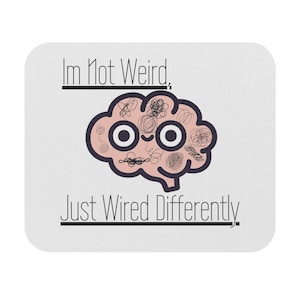 May include: A white square mouse mat featuring the text "Im Not Weird, Just Wired Differently." A cartoon brain with large eyes and scribbled details is in the center. The brain is pink with black outlines.