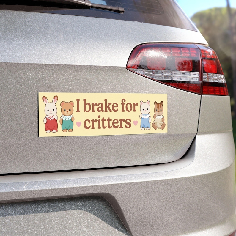 Może przedstawiać: Prostokątna naklejka na zderzak z napisem "I brake for critters" w brązowej czcionce na jasnym ż&oacute;łtym tle. Naklejka zawiera ilustracje kresk&oacute;wkowe kr&oacute;lika, misia, kota i wiewi&oacute;rki.
