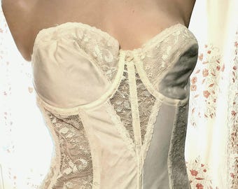 May include: Ivory-colored strapless corset with lace detailing. The bodice features a sweetheart neckline and a vertical zipper closure. The corset is displayed on a mannequin, showcasing its vintage design.