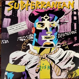 May include: Album cover for "Subterranean" featuring a stylized, colorful illustration of a figure with a mask and a yellow shirt with the word "Risk". The cover includes text that reads "The Residents" and "Chrome-MX-80 Sound-Tuxedomoon".