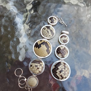 May include: A silver bracelet featuring circular, snake-skin patterned accents. The bracelet has a toggle clasp and a series of connected, round charms with a reptile scale design in shades of brown, tan, and black.