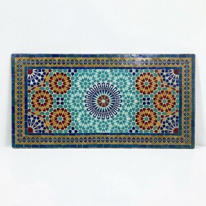K&ouml;nnte beinhalten: Eine rechteckige Tischplatte mit einem komplexen Mosaikmuster aus kleinen, handgeschnittenen Fliesen in T&uuml;rkis, Dunkelblau, Senfgelb und Dunkelrot. Das Design zeigt ein zentrales Sternmotiv, das von sich wiederholenden geometrischen Mustern umgeben ist.