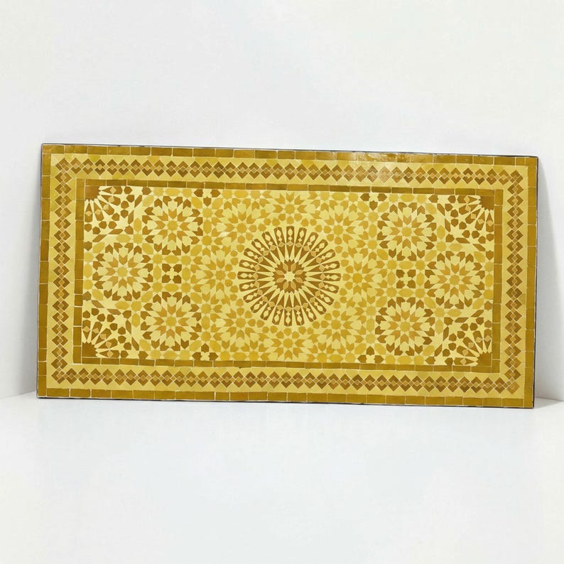 K&ouml;nnte beinhalten: Eine rechteckige Tischplatte mit einer Mosaikoberfl&auml;che aus kleinen, handgeschnittenen Fliesen in verschiedenen Gelb- und Goldt&ouml;nen. Das Design zeigt ein zentrales Sternmuster, umgeben von sich wiederholenden geometrischen Motiven und einer Umrandung.
