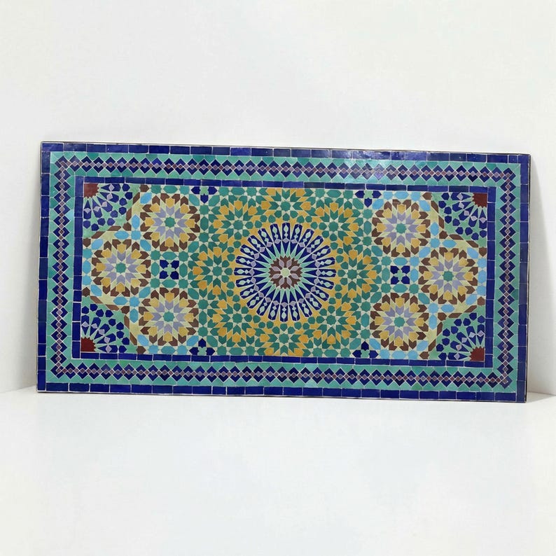K&ouml;nnte beinhalten: Eine rechteckige Mosaik-Tischplatte mit einem komplexen geometrischen Muster aus kleinen Fliesen in den Farben Dunkelblau, T&uuml;rkis, Gelb und Wei&szlig;. Das Design umfasst ein zentrales Sternmotiv, das von sich wiederholenden Stern- und Polygonformen umgeben ist.
