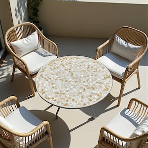 May include: A patio set featuring a round table with a mosaic tile top and four wicker chairs. Each chair has a white cushion and pillow. The table has a metal frame and the chairs are made of light brown wicker.