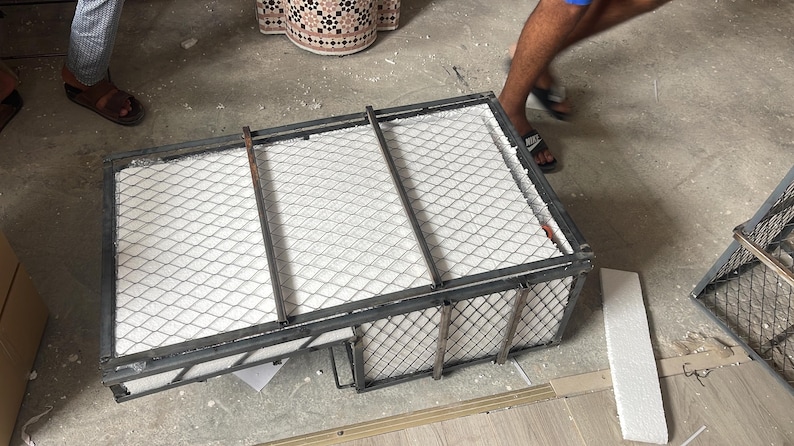 Puede incluir: Un marco met&aacute;lico rectangular con una parte superior de malla de alambre y material blanco en el interior. El marco est&aacute; sobre un suelo de hormig&oacute;n. Una persona est&aacute; de pie cerca.
