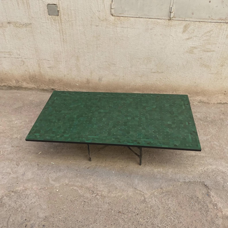 Puede incluir: Una mesa de centro rectangular con una superficie plana cubierta por un patr&oacute;n de mosaico verde oscuro de peque&ntilde;as baldosas cuadradas. La mesa est&aacute; sostenida por una estructura de metal negro con cuatro patas delgadas y anguladas.