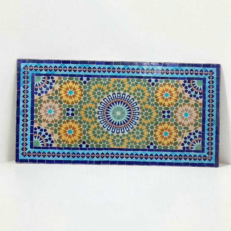 K&ouml;nnte beinhalten: Eine rechteckige Mosaikfliesenplatte mit einem komplexen geometrischen Muster. Das Design umfasst ein zentrales kreisf&ouml;rmiges Medaillon, das von sich wiederholenden sternf&ouml;rmigen Motiven in den Farben Dunkelblau, T&uuml;rkis, Olivgr&uuml;n und Goldgelb umgeben ist.
