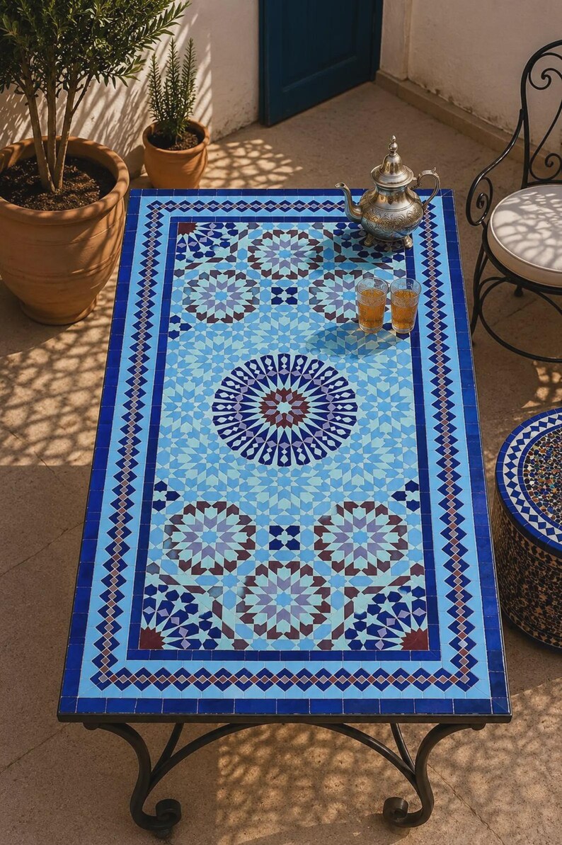 K&ouml;nnte beinhalten: Ein rechteckiger Tisch mit einer Mosaik-Tischplatte mit komplexen geometrischen Mustern in Hellblau, Dunkelblau und Braun. Der Tisch steht auf einem schwarzen Metallgestell mit geschwungenen Beinen und ist mit einer silbernen Teekanne und zwei Gl&auml;sern versehen.