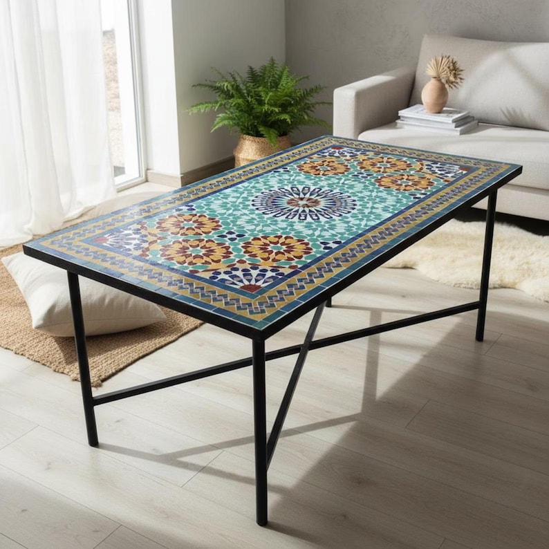 K&ouml;nnte beinhalten: Ein rechteckiger Couchtisch mit einer Mosaik-Tischplatte, die komplexe geometrische Muster in Blaugr&uuml;n, Gelb, Orange und Dunkelblau aufweist. Der Tisch wird von einem schlichten schwarzen Metallrahmen mit vier d&uuml;nnen Beinen und Querstreben getragen.