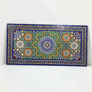 K&ouml;nnte beinhalten: Eine rechteckige Tischplatte mit einem komplexen Mosaikmuster aus kleinen, handgeschnittenen Fliesen in den Farben Dunkelblau, Waldgr&uuml;n, Senfgelb, Wei&szlig; und Braun, das ein zentrales Sternmotiv und verschiedene geometrische Formen aufweist.