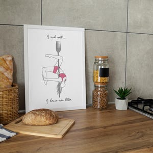 Könnte beinhalten: Ein weißer gerahmter Druck mit einer Schwarzweißillustration einer Frau, die auf einer Gabel tanzt. Der Text auf dem Druck lautet "Ich koche gut... Ich tanze noch besser."