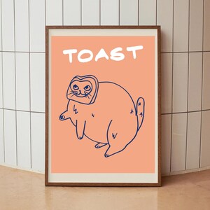 Puede incluir: Un póster de color melocotón con la palabra "TOAST" en texto blanco en la parte superior. Un dibujo de línea azul de un gato que lleva una rebanada de pan como sombrero está en el centro del póster.