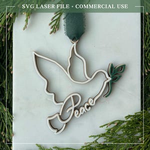 May include: A wooden dove ornament with the word "Peace" in script. The dove is outlined in a light brown color with white accents. A green ribbon is attached for hanging. The text "SVG LASER FILE + COMMERCIAL USE" is at the top.
