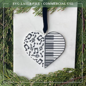 May include: A heart-shaped decoration with a black ribbon. One half is covered in musical notes, the other has a piano keyboard design. The ornament is white with black detailing. The text at the top reads "SVG LASER FILE + COMMERCIAL USE."