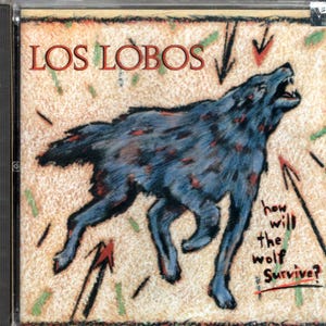 May include: CD case featuring the band name "LOS LOBOS" in red letters. A blue wolf with red spots is howling, surrounded by arrows and the text "how will the wolf Survive?" on a beige background.