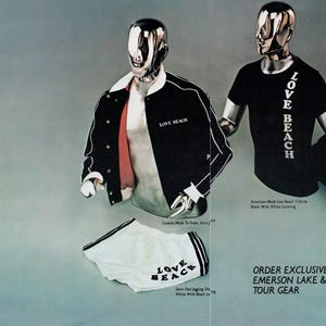 K&ouml;nnte beinhalten: Schwarze und wei&szlig;e Satinjacke mit rotem Futter und "Love Beach" Stickerei auf der Vorderseite. Schwarzes T-Shirt mit "Love Beach" vertikal auf der Vorderseite bedruckt. Schwarze Jacke mit wei&szlig;em Streifen und "Emerson Lake & Palmer" auf der R&uuml;ckseite bedruckt. Wei&szlig;e Satin-Shorts mit schwarzem Besatz und "Love Beach" auf der Vorderseite bedruckt. Exklusiv bestellbare Emerson Lake & Palmer Tour-Ausr&uuml;stung.