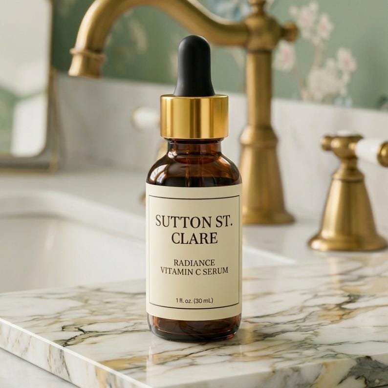 May include: A brown glass bottle of Sutton St. Clare Radiance Vitamin C Serum with a black dropper and gold cap. The label is cream-coloured with black text. The bottle is on a marble surface near a gold tap.