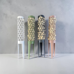 May include: Four cylindrical plant moss poles with a hexagonal honeycomb pattern. The poles are white, olive green, dark gray, and dusty pink. Three of the poles are filled with light-colored dried moss, while the white pole is empty.