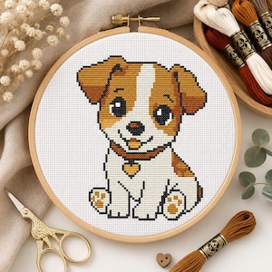 May include: A cross-stitch embroidery project in a round wooden hoop featuring a white and tan puppy with large black eyes, a small heart-shaped tag on its collar, and tan paw pads, displayed on a white fabric background with visible grid stitches.