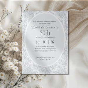 May include: A formal invitation for a 20th wedding anniversary. The design features a silver oval frame with floral patterns and text that reads "Emma & Daniel's 20th Wedding Anniversary". The date is October 3, 2026. The invitation includes RSVP details.