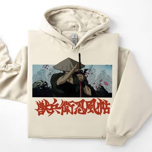 May include: Cream-colored hoodie featuring a graphic of a samurai holding a sword, set against a backdrop of a wave and floral design. Red Japanese text is printed below the graphic. The hoodie has a drawstring hood and a kangaroo pocket.