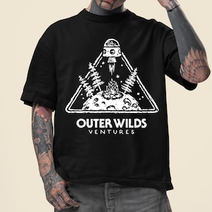 Może przedstawiać: Czarny t-shirt z białą grafiką przedstawiającą statek kosmiczny startujący z planety, otoczony drzewami i ogniskiem, w trójkącie. Pod grafiką znajduje się napis "OUTER WILDS VENTURES".