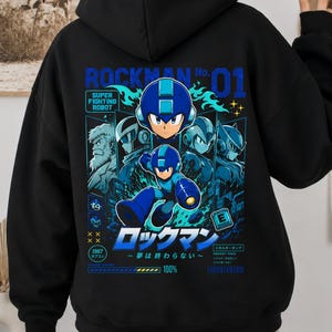 May include: A black hooded sweatshirt featuring a large graphic on the back with the text ROCKMAN No. 01. The design includes blue and white illustrations of the character Rockman, various robotic figures, and Japanese text, with an energy tank icon.